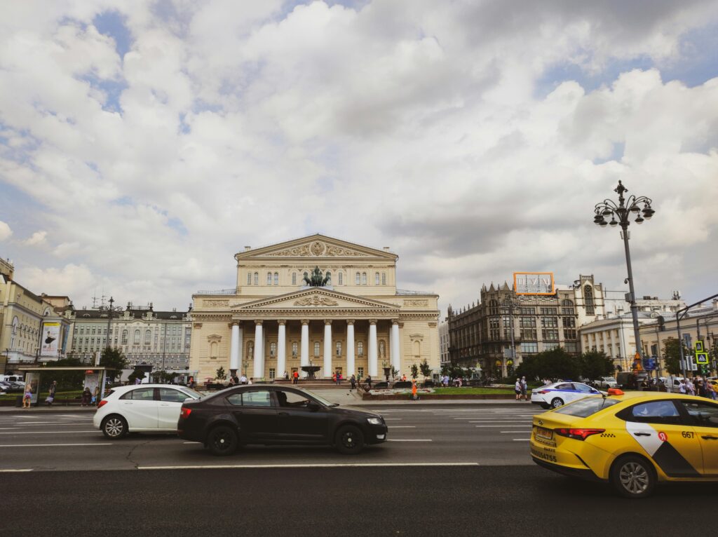 View of the iconic Bolshoi Theatre with bustling street and traffic in Moscow.