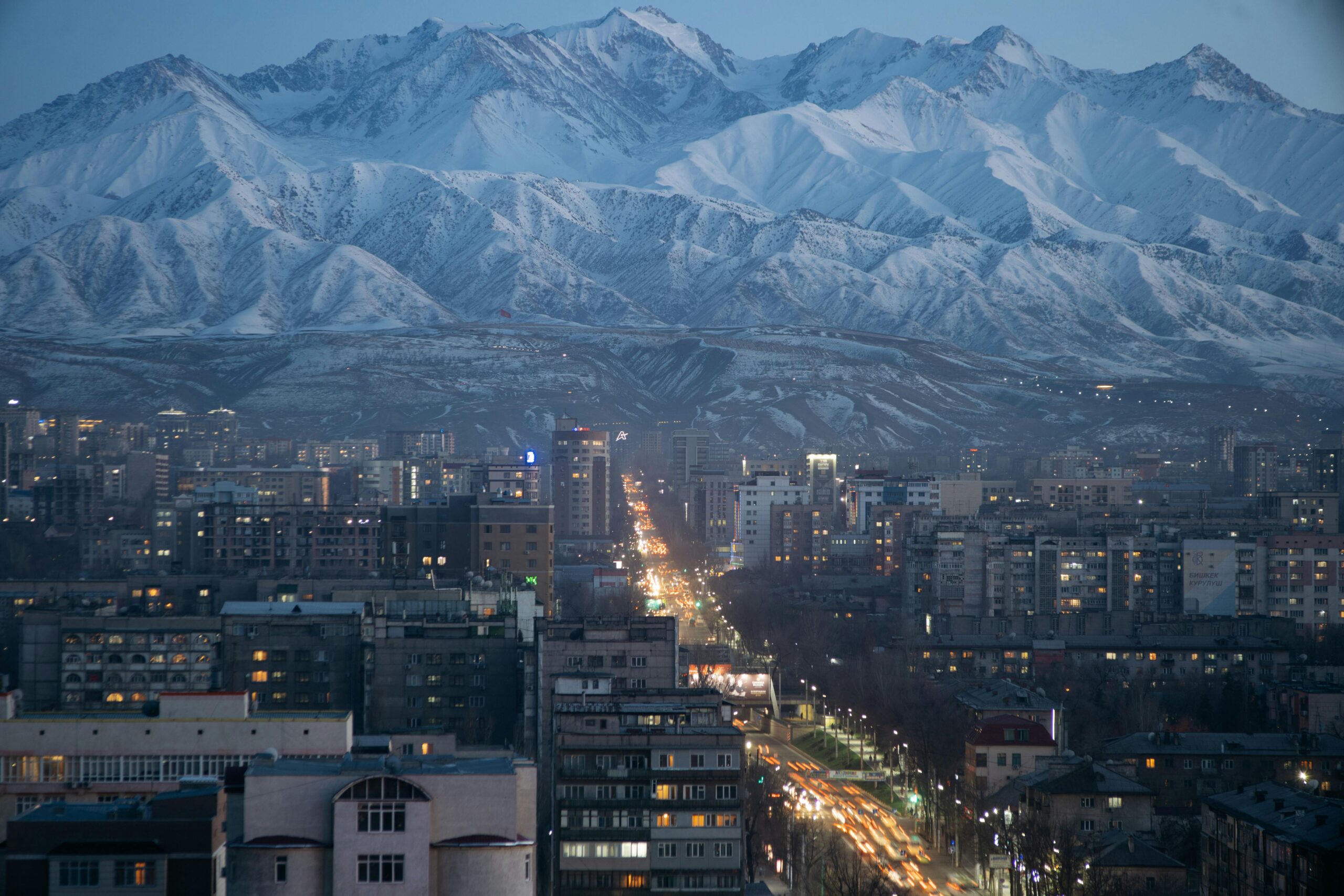 A breathtaking view of Bishkek with snow-capped mountains at twilight, showcasing its urban skyline and natural beauty.