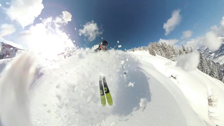 Exciting skiing action captured mid-air with snowy splash and bright sunny backdrop.