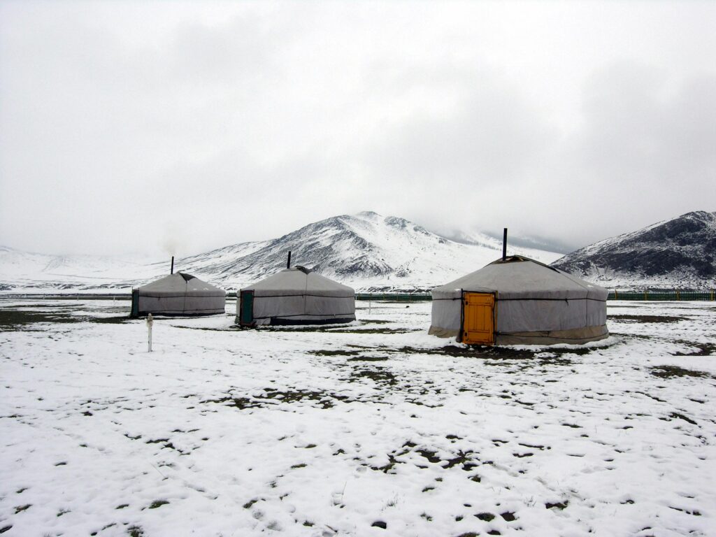 A peaceful winter scene with traditional yurts in a snowy mountainous setting.