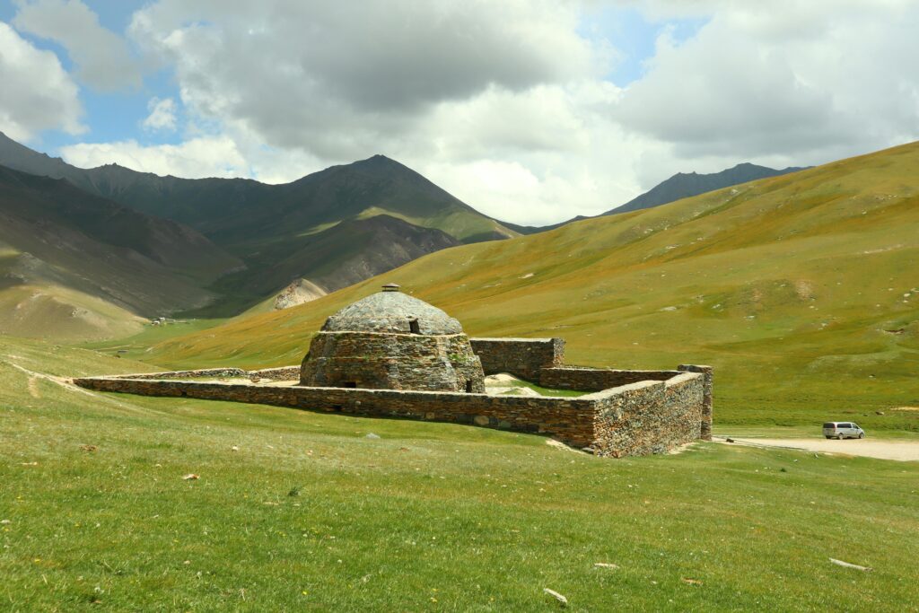 Tash Rabat caravanserai amidst lush Kyrgyz mountains under a cloudy sky.