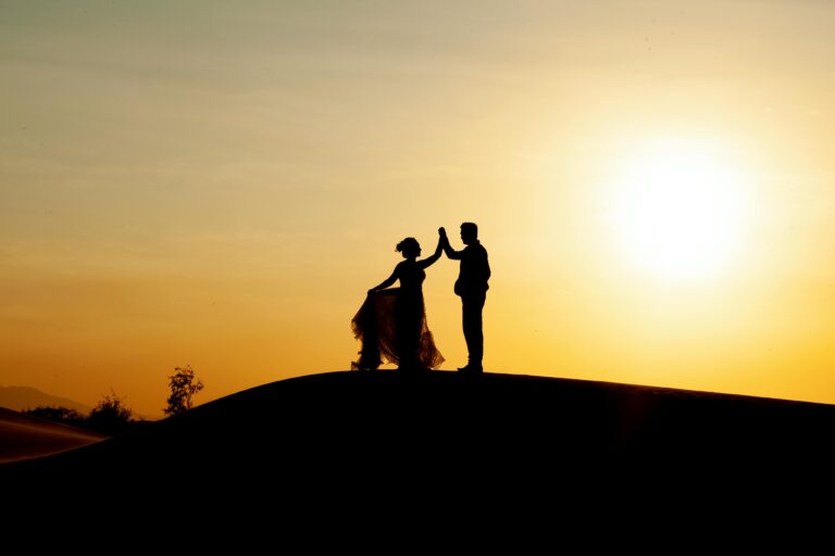 Silhouetted couple dancing on the beach during a golden sunset, creating a romantic scene.