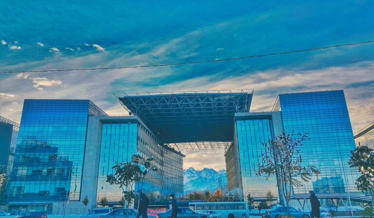 Rascacielos contemporáneo de vidrio con montañas en Almaty enmarcadas por cielos azules.