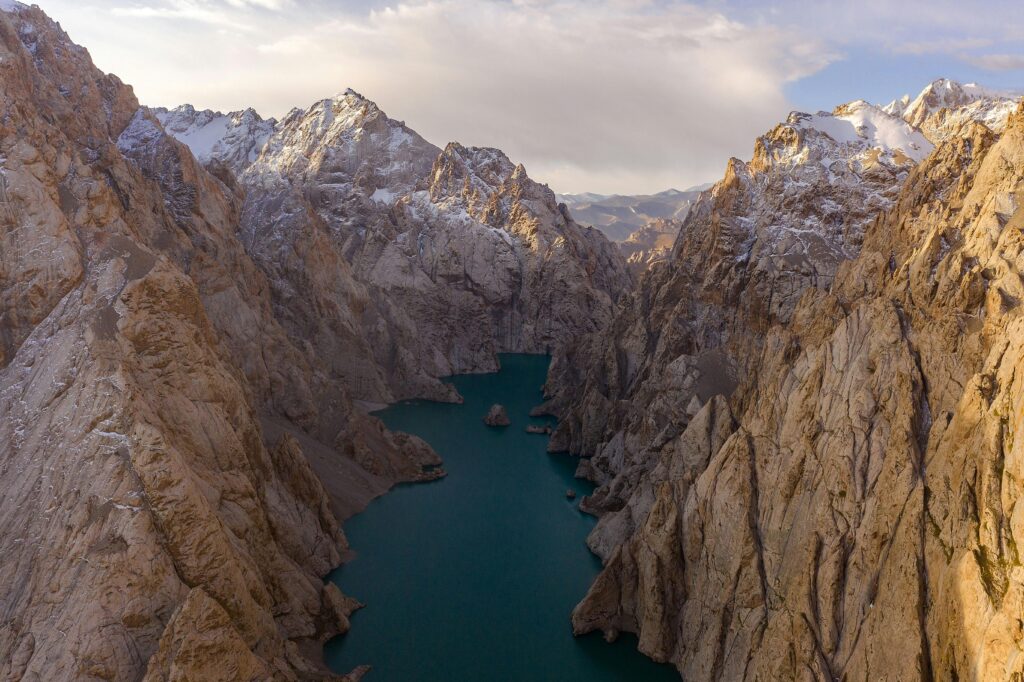 Dramatic aerial view of Kol Suu Lake surrounded by rugged mountains in Kyrgyzstan, showcasing natural beauty and serenity.