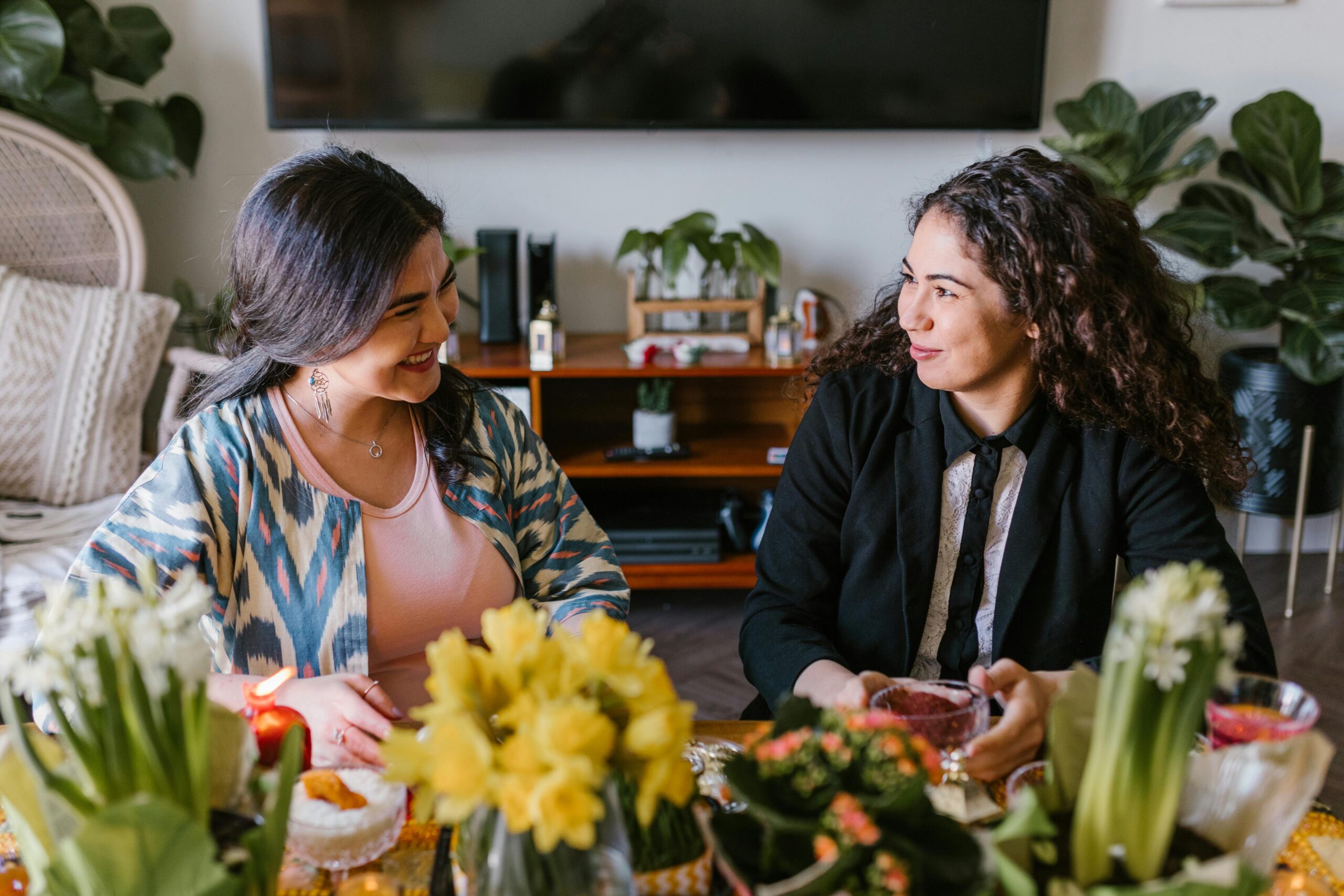 Two women enjoying a traditional Persian New Year celebration indoors with vibrant decorations and smiles.
