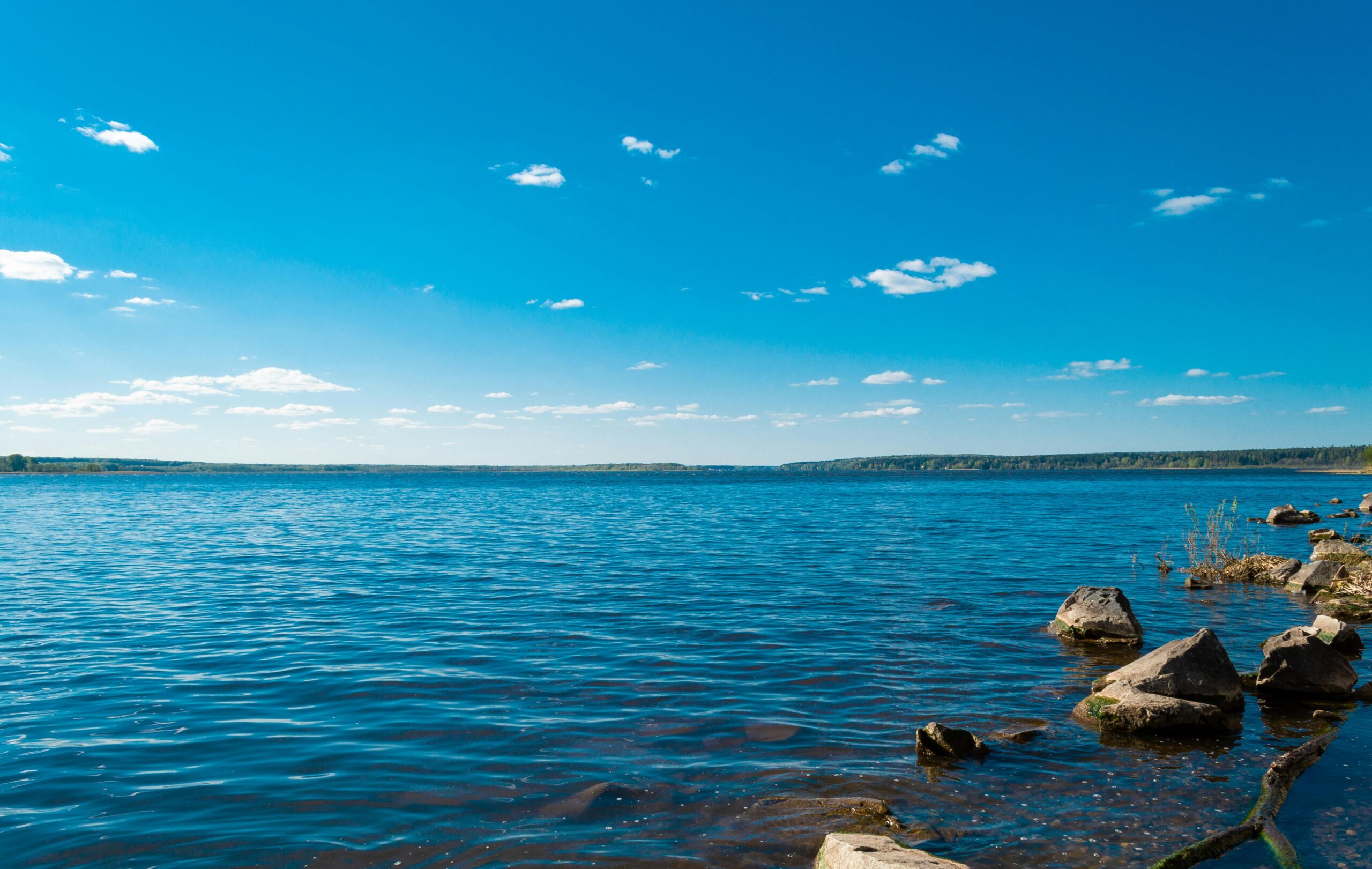 Serene view of a blue lake with rocky shore under a clear blue sky, ideal for nature lovers.