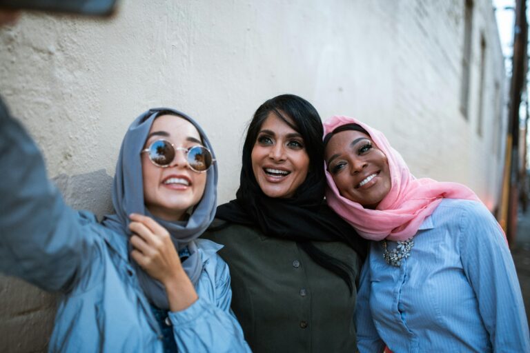 Three smiling women in colorful hijabs take a selfie outdoors, showcasing diversity and friendship.