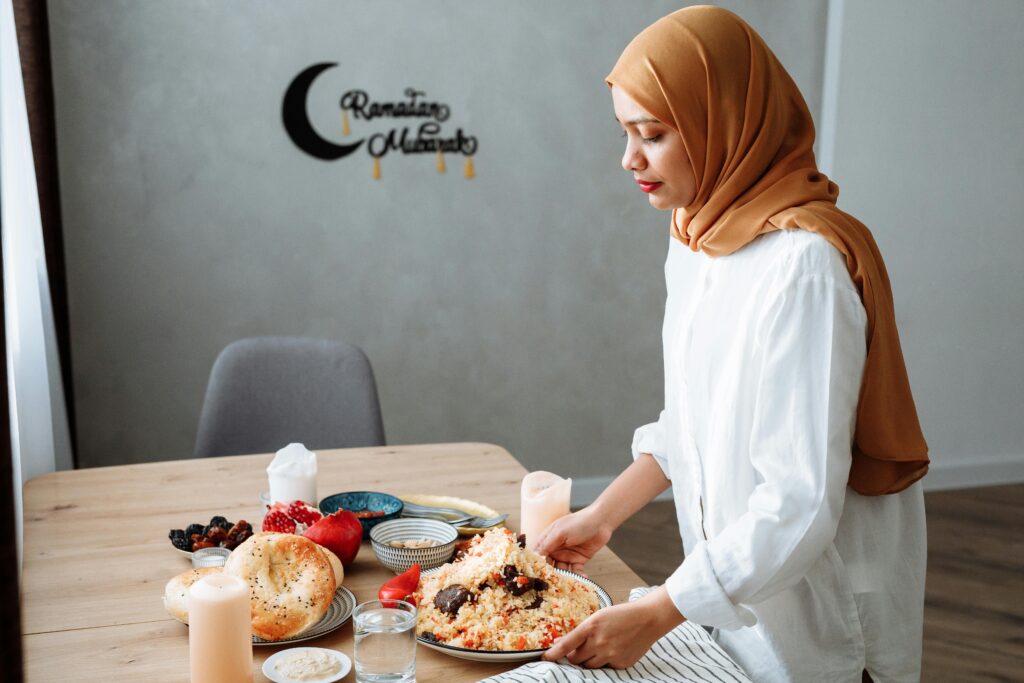 Muslim woman in hijab setting table with traditional iftar food during Ramadan.