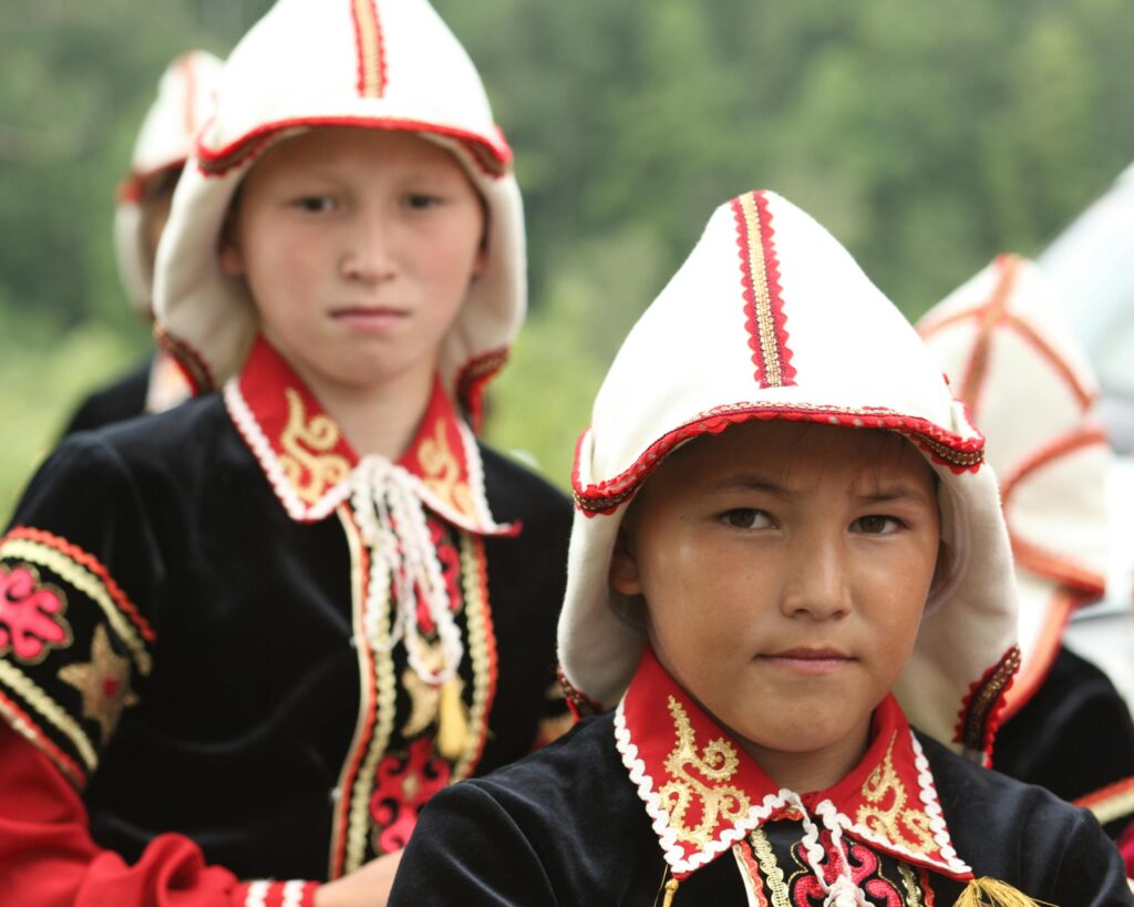 Children in vibrant traditional Kyrgyz costumes participating in a cultural festival outdoors.