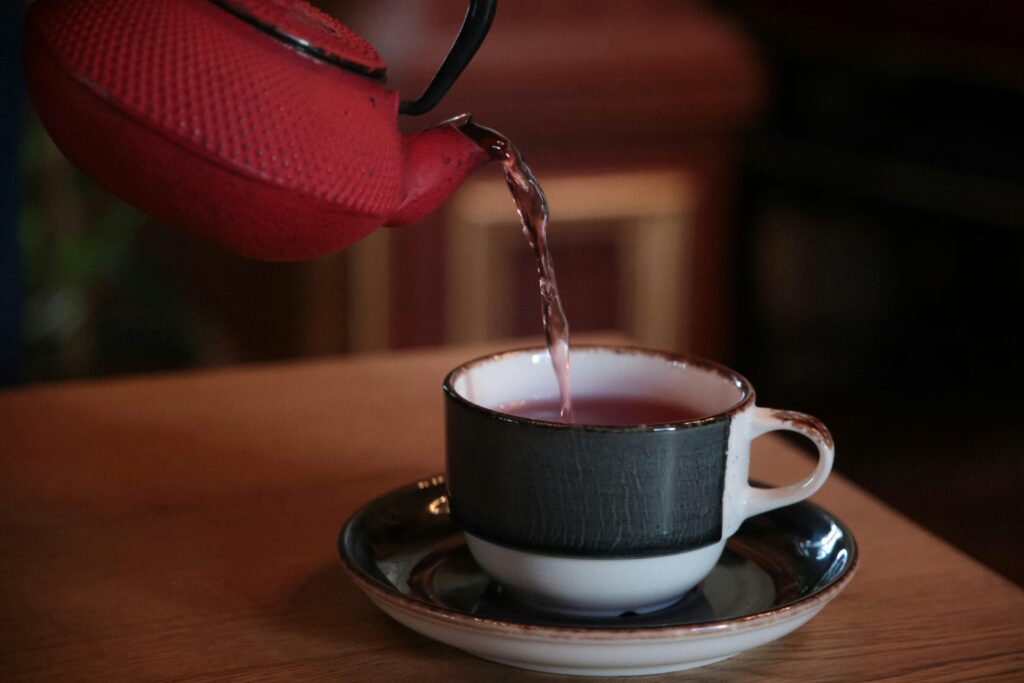 Red kettle pouring tea into a stylish cup on a wooden table, creating a cozy atmosphere indoors.