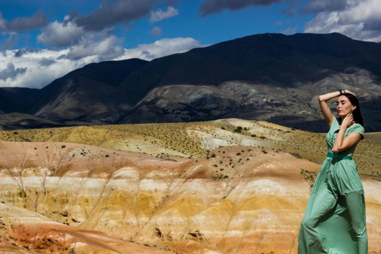 A woman in a green dress poses against the colorful landscapes of the Altai Mountains.