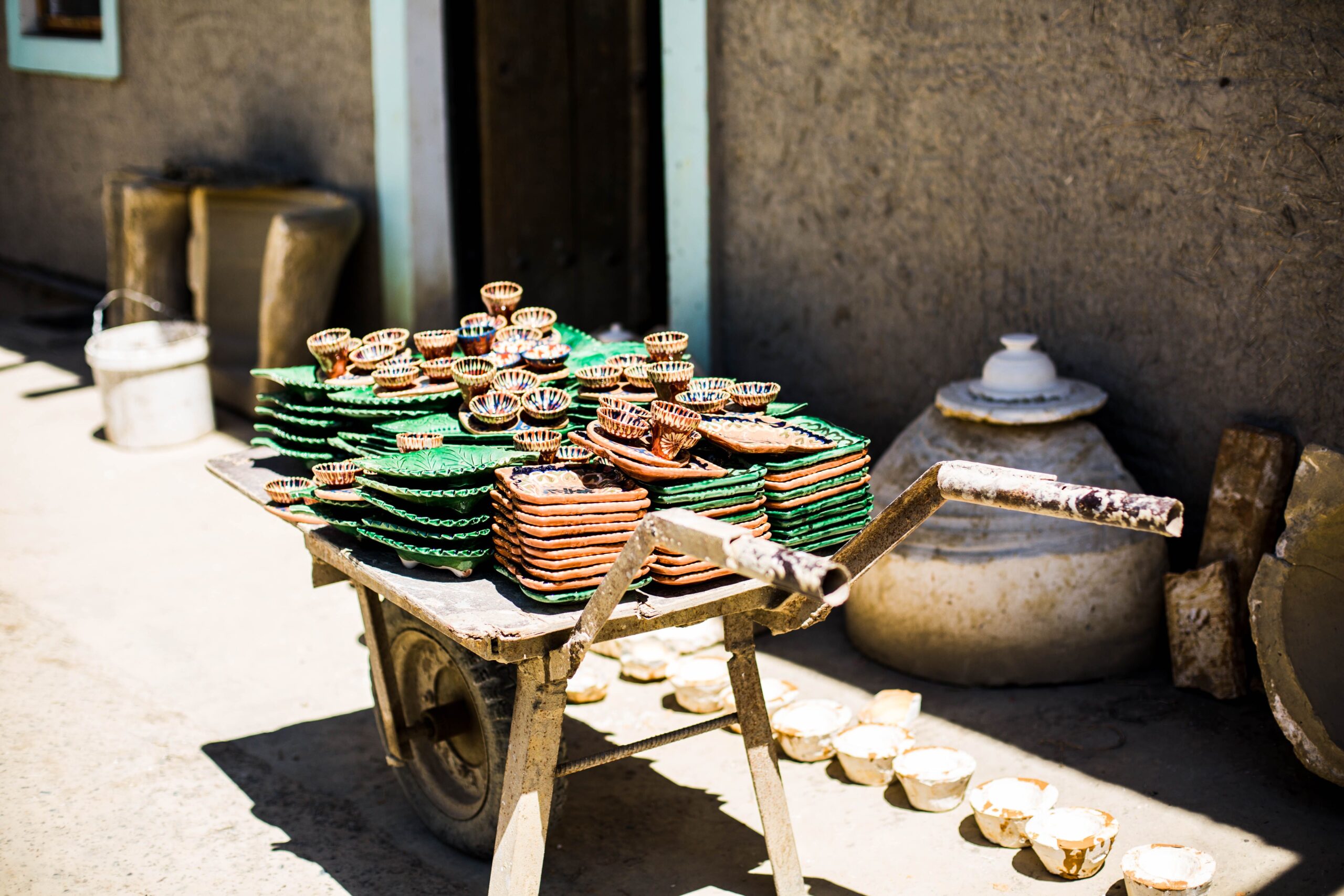 Vibrant clay pots displayed on a wheelbarrow outdoors in Gijduvon, Uzbekistan.