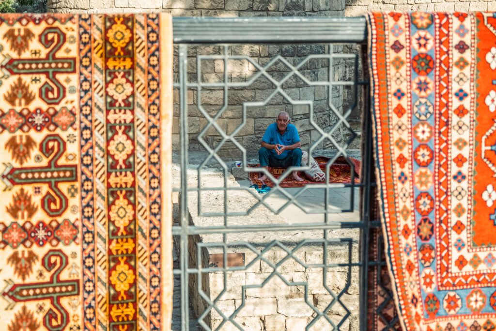 Elderly man seated in old town Baku, Azerbaijan, framed by traditional carpets and architecture.