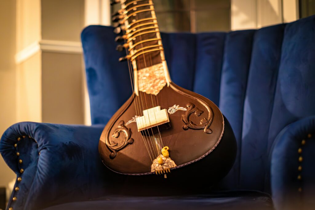 A beautifully crafted sitar resting on a plush blue velvet chair in a cozy room.