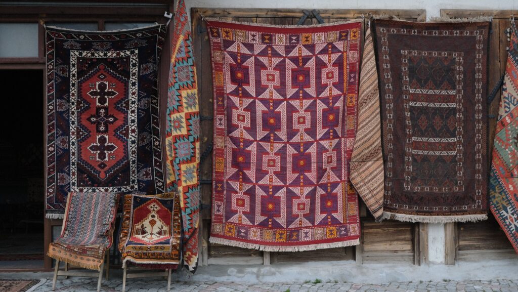 Vibrant collection of traditional rugs hanging outside a shop showing intricate patterns.