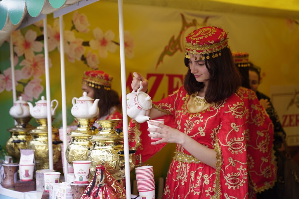 Young woman in traditional attire serving tea at a vibrant cultural festival. Captivating scene.