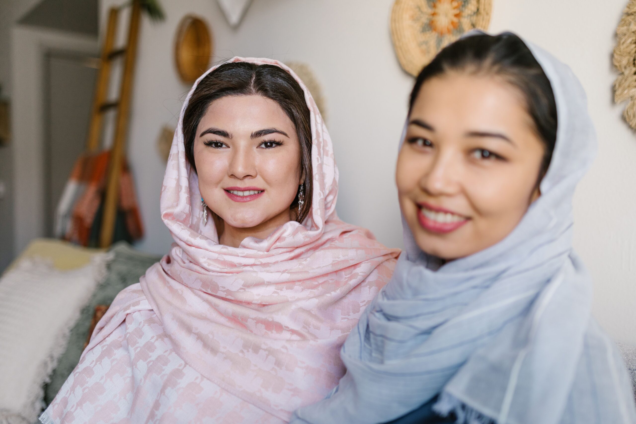 Two women in traditional scarves sharing a joyful moment indoors during Nowruz.