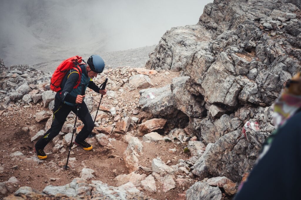 A determined hiker conquering a rocky mountain trail with trekking poles and helmet, showcasing adventure.