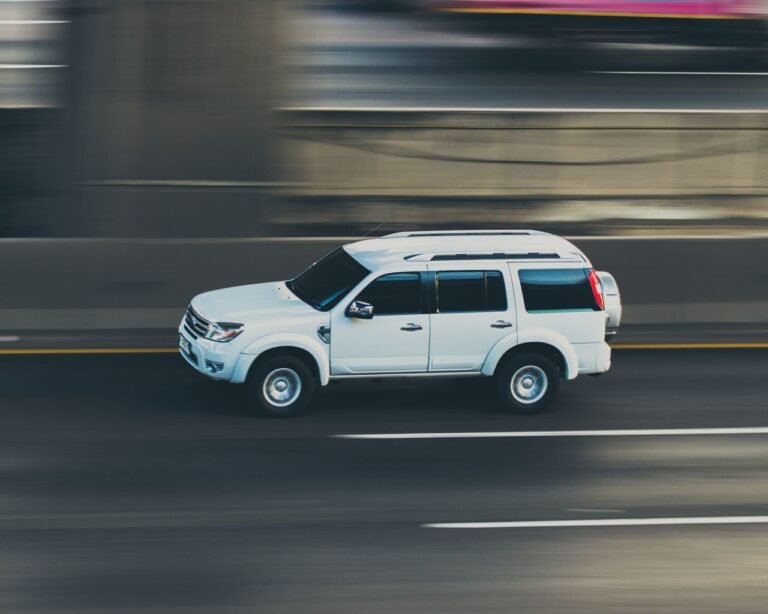 A white SUV captured in a dynamic panning shot speeding on a highway during the day.