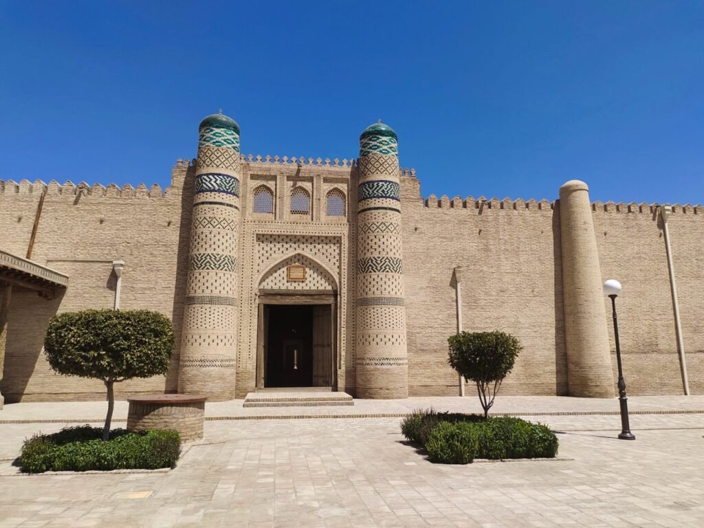 Majestic fortress entrance with intricate minarets under a vibrant blue sky in Bukhara, Uzbekistan.