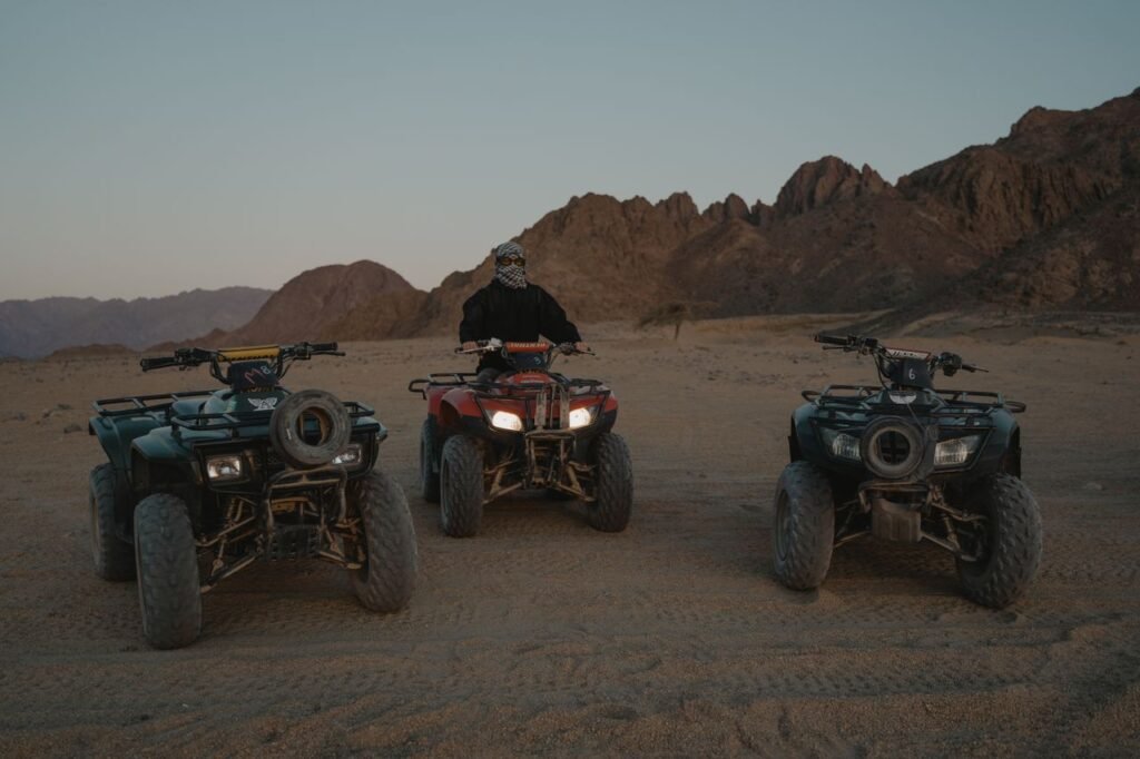 A person sits on an ATV in a rugged desert surrounded by mountains.