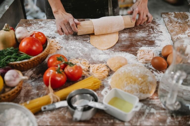 Crop anonymous female cooking homemade pasta on table covered with flour among vegetables